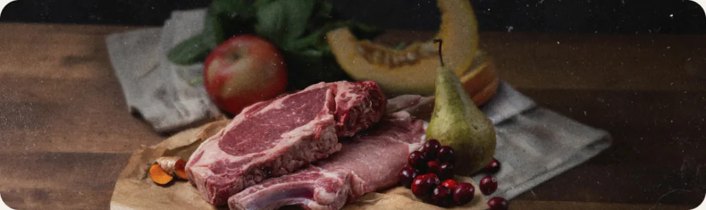 Raw steaks with an apple, a pear, cranberries and squash on a wooden board