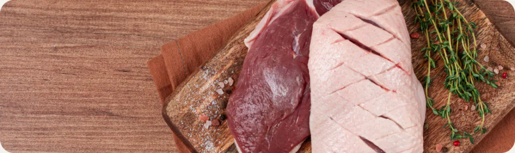 Raw red meat and a scored poultry breast on a wooden board with fresh thyme