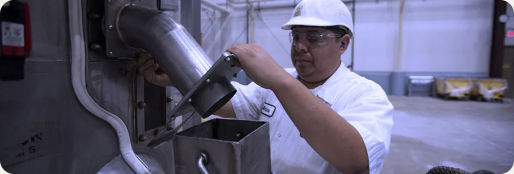 A worker in a hard hat and safety glasses checking equipment in a production plant